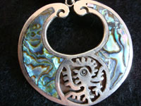 Closeup of vintage Mexican silver earrings with abalone and Aztec design.