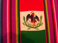 Mexican vintage textiles and sarapes, a textile or sarape woven of fine wool and representing the Mexican flag and national symbol of the eagle with snake, c. 1940. The piece bears the traditional colors of the Mexican flag: red, green, and white. Closeup photo of the eagle on the front of the sarape.