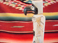 Native American Indian antique folk art, a carved, bone totem pole from Alaska, c. 1920-30's. The figure of the Raven with outstretched wings (the mythical hero of the Tlingit) hovers at the top of the pole, sheltering the three children of the sun. Closeup photo from the side, showing the Raven and its beak.