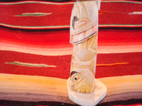 Native American Indian antique folk art, a carved, bone totem pole from Alaska, c. 1920-30's. The figure of the Raven with outstretched wings (the mythical hero of the Tlingit) hovers at the top of the pole, sheltering the three children of the sun. Side view of the bottom figures on the pole.