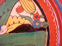Mexican vintage pottery and ceramics, a wonderful charger from Tlaquepaque, c. 1930-40. Beautifully decorated with a Diego Rivera-like scene of a woman kneeling as she contemplates lovely flowers. Closeup photo of the lovely plants and leaves on the upper left front of the charger.
