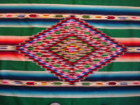 Mexican vintage textiles and sarapes, a stunning Saltillo sarape with silk and real silver threads in the center diamond, c. 1920-30. The decorative end-bars on each side feature lovely rosettes and the fringe is fully intact on each end. Closeup photo of the center diamond of the Saltillo sarape.
