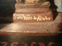 Mexican vintage devotional art, and Mexican vintage folk art, a wooden nicho with a bulto (carved wooden statue) of the Santo Nino de Atocha, c. 1940. This is a beautiful piece of vintage Mexican fine/folk art! Closeup photo of the base of the nicho with the title, Santo Nino de Atocha.