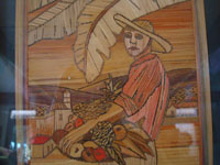 Close-up photo of straw-art picture of man with basket of fruit.